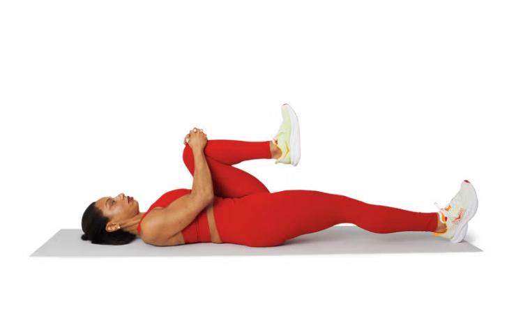 Een vrouw ligt op een yogamatje en voert de Lying Hip Flexor Stretch uit